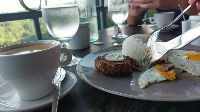 Low angle view close up to a plate of frikadeller or beef patty, fried egg and rice being eaten for a hearty breakfast and healthy morning routine