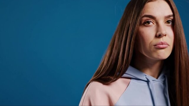 Young woman reacts to bad smell by pinching her nose and wincing in disgust against blue background with humorous and expressive body language

