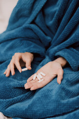 Person wrapped in blue blanket holding white pills in both hands
