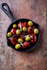 Fried sausages with green olives and rosemary in cast-iron pan