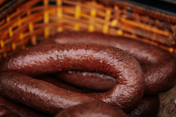 Close-up of blood sausages with grains in a coiled arrangement inside a woven basket, showcasing their dark, glossy texture and traditional preparation style.