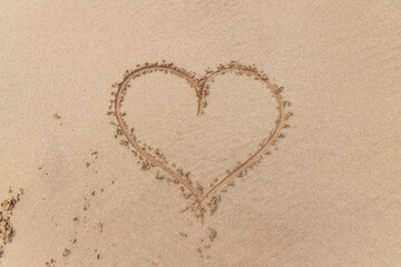 Ceannabeinne Beach shines under a clear summer sky. Crystal-clear waters, golden sand with a heart drawn on it, and lush green grass create a pristine and romantic coastal escape.