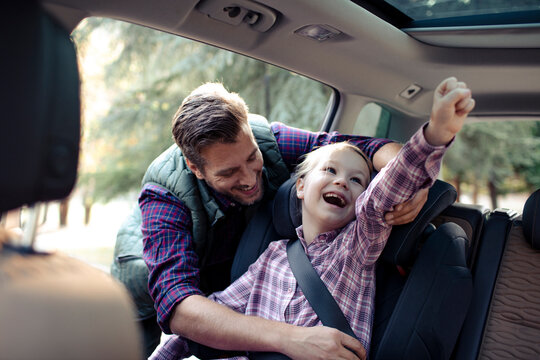Father securing daughter in car seat before family road trip
