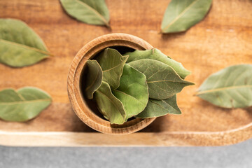 Fresh bay leaves in a wooden bowl surrounded by dried leaves on a kitchen table