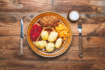 Minced cutlet, boiled potatoes, beets and fresh vegetables served on a wooden table.