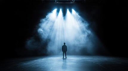 A solitary figure stands illuminated under dramatic stage lighting
