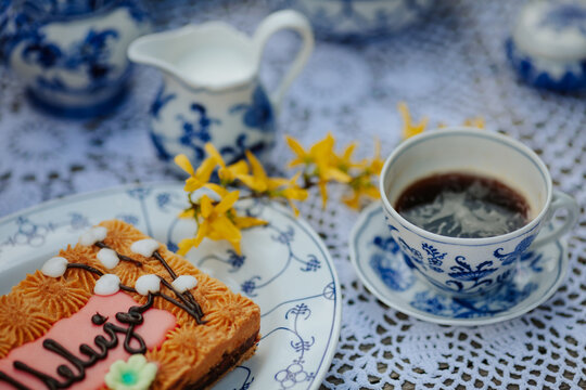 Cup of hot coffee with mazurek cake on a porcelain plate with a jug of milk and yellow flowers on Easter morning