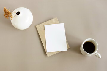 Blank card mockup , envelope, vase with dry flowers and coffee cup top view on beige background template . Greeting card mock up.Neutral colors minimalist workplace background.
