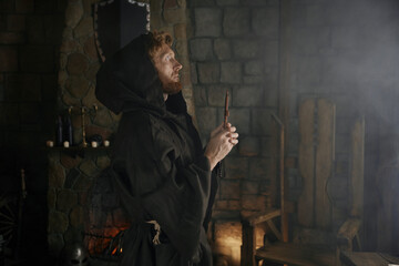 Faithful priest in robe hood praying with rosary beads and cross