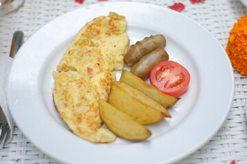 Delicious and Hearty Breakfast Plate: Omelette, Sausages, Potato Wedges, and Tomato