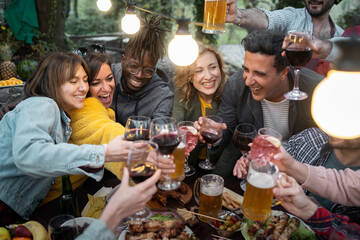 Diverse group of happy friends toasting with wine and beer at outdoor dinner party