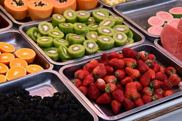 Various fruits in metal serving trays, including strawberries, kiwi, oranges, papaya, and watermelon.