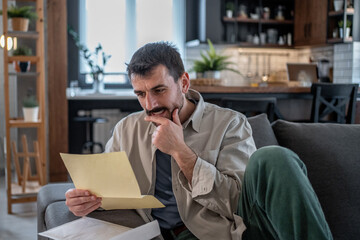 Pensive man reading important documents on sofa at home