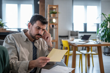 Worried man reading a letter and thinking about bills at home