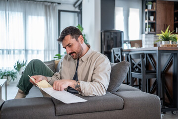 Focused entrepreneur reading documents while sitting on sofa at home