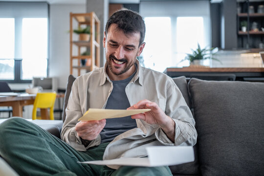 Happy man opening envelope and reading good news at home