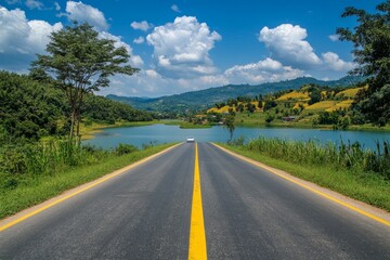 Fototapeta premium Scenic asphalt road leading to a tranquil lake nestled amidst rolling hills under a vibrant sky