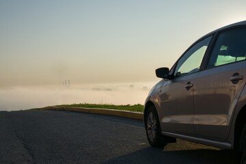 A clean, new car is parked on the side of the road on a mountain against the backdrop of a city in the fog