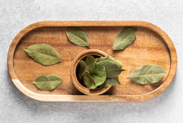 Bay leaves arranged on a wooden tray with a bowl of dried leaves in the center