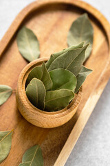 Fresh bay leaves in a wooden bowl on a natural wood tray for culinary uses