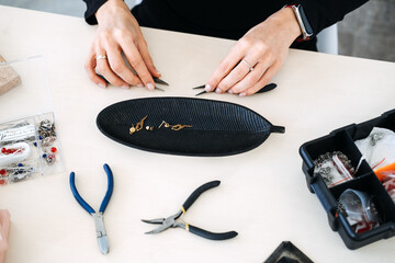Close-up of jewelry maker assembling a gold earring shaped like a dancer using precision pliers....