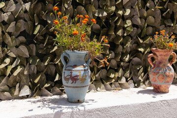Two hand-painted ceramic vases with bright orange flowers sit on a white ledge in sunlight on a Greek island.