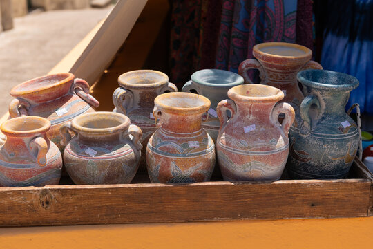 A collection of hand-painted Greek vases displayed in a wooden crate at a local artisan market under the sun.