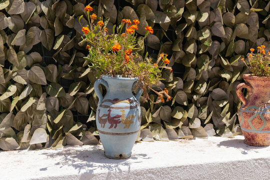 A hand-painted ceramic vase with orange marigold flowers basks in sunlight on a Greek island patio. - Powered by Adobe
