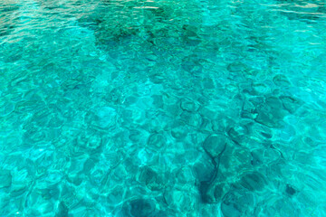 Close-up of crystal clear turquoise water with gentle ripples and sunlit reflections from the Greek islands.