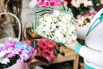 Florist reaching for bouquet of chamomile at display table. Highlights sustainable floristry, no foam bouquets, and local flower sourcing