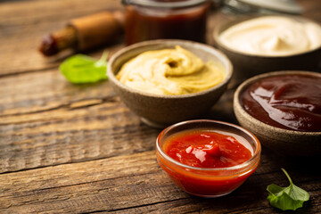 Classic set of sauces, American yellow mustard, ketchup, barbecue sauce, mayonnaise on wooden background, top view with copy space.