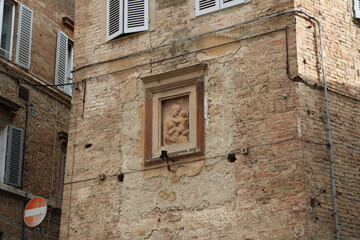Ancient sculpture of Holy Mary and baby Jesus in a wall of a medieval house in Siena, Italy.