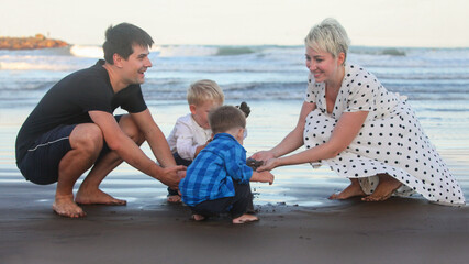 Fototapeta premium portrait of cheerful young couple with two little boys on the beach at dusk by the ocean bonding 