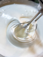 Electric hand mixer whipping egg whites in a bowl to form stiff peaks. Close-up of the foamy texture during mixing.