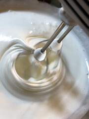 Electric hand mixer whipping egg whites in a bowl to form stiff peaks. Close-up of the foamy texture during mixing.