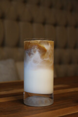 A perfectly layered iced latte with visible ice cubes served in a tall transparent glass, showcasing an ideal blend of cold milk and espresso sitting on a polished wooden table inside a cozy modern