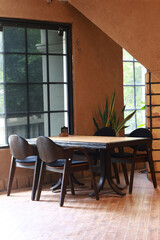 Cozy rustic indoor café corner featuring wooden tables, vintage chairs, large glass windows, and earthy wall textures. Natural daylight floods the room, creating a peaceful, warm, and inviting