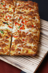 Rectangular pizza with vibrant toppings served with rich dipping sauces on a rustic wooden board, featuring golden crispy edges, colorful peppers, and gooey melted cheese, ideal for food promotions