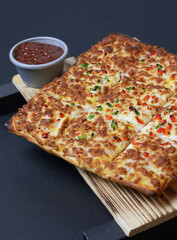 Rectangular pizza with vibrant toppings served with rich dipping sauces on a rustic wooden board, featuring golden crispy edges, colorful peppers, and gooey melted cheese, ideal for food promotions