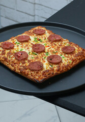 Square pepperoni pizza with golden crispy crust and melted cheese served on a dark plate, featuring fresh herbs and vibrant toppings, ideal for fast food menus, restaurant promotions, casual dining ad
