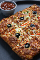 Sliced cheesy pizza with colorful vegetable toppings on a rustic wooden tray served with tomato...