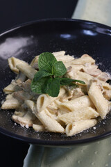 Creamy white sauce penne pasta served with a lemon wedge and fresh mint garnish in a black bowl, showcasing a hearty and rich Italian dish perfect for restaurant menus and gourmet food promotions.