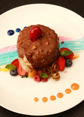 Artistic chocolate dessert with a rich chocolate shell and colorful sauce decorations, beautifully presented with fresh berries and mint leaves on a white plate, ideal for fine dining menus and luxury