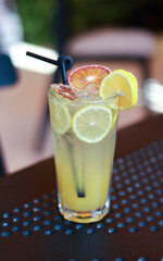 Fresh and vibrant citrus drink served in a tall glass, decorated with dried orange slices and a black straw, placed on a modern outdoor metal table with bright natural light and soft blurred backgroun