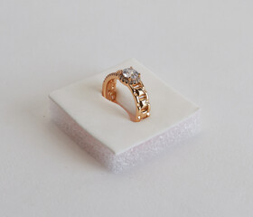 Luxurious gold ring with a floral-inspired design featuring multiple dazzling crystal flowers, meticulously handcrafted and elegantly displayed on a white foam platform, captured against a clean brigh