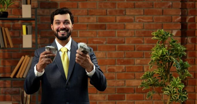 Holding currency notes confidently, Indian businessman displays bunch of five hundred rupee bills. Asian CEO or entrepreneur in corporate attire stands in cozy office with terracotta brick wall