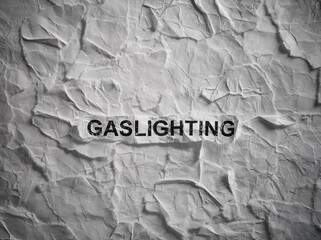 Crumpled piece of paper with word Gaslighting on torn white paper pieces background.