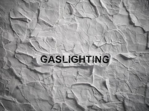 Crumpled piece of paper with word Gaslighting on torn white paper pieces background.