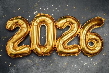 Golden balloons shaped like the year 2026 with confetti on a dark background © reddish