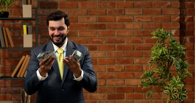 Holding currency notes confidently, Indian businessman displays bunch of five hundred rupee bills. Asian CEO or entrepreneur in corporate attire stands in cozy office with terracotta brick wall